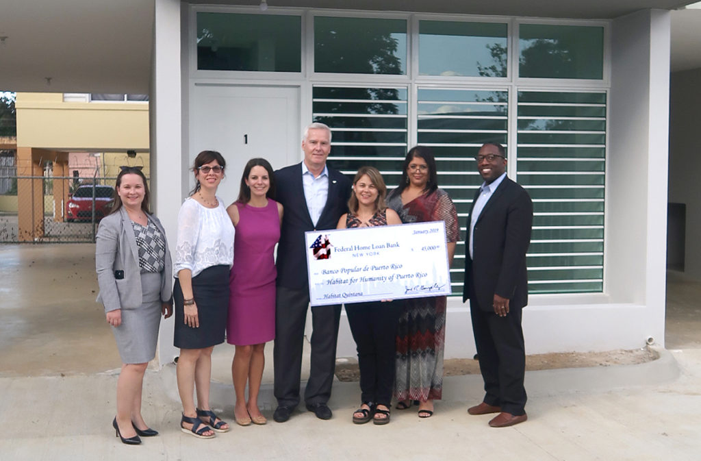 Staff from the FHLBNY, Banco Popular, and Habitat for Humanity stand with a check in front of a building